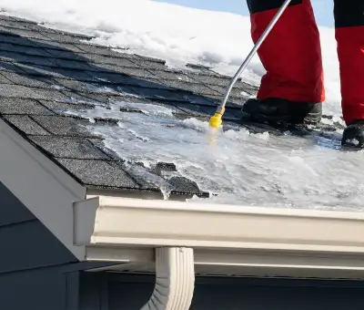 Ice dam removal technician using a steam wand to melt thick ice buildup on a residential roof in ,
