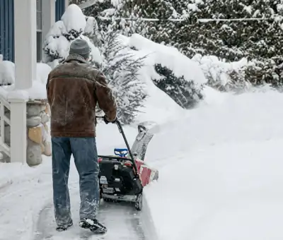 Residential snow removal technician using a snow blower to clear a home driveway and walkway in ,